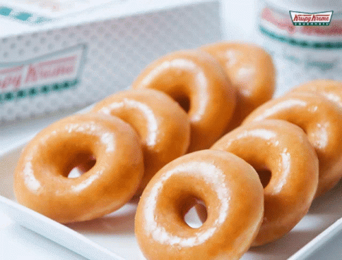 A Box Of Krispy Kreme Donuts Sits Next To A White Plate Of Donuts GIF