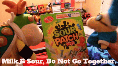 A Box Of Post Sour Patch Kids Cereal With Two Stuffed Animals Standing Next To It GIF