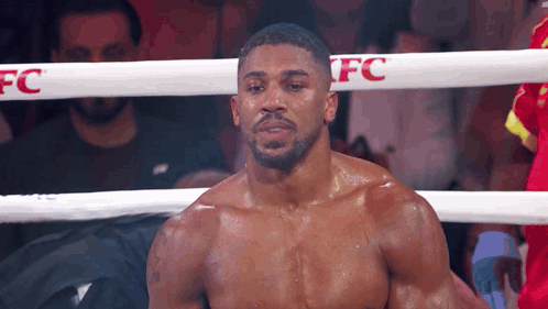 A Boxer Without A Shirt Is Standing In A Boxing Ring Looking At The Camera . GIF