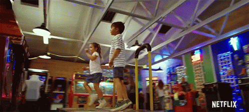 A Boy And A Girl Are Jumping On A Dance Floor In An Amusement Park . GIF
