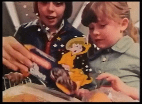 A Boy And A Girl Are Sitting At A Table Playing With A Cartoon Character . GIF