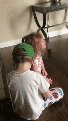 A Boy And A Girl Are Sitting On A Wooden Floor GIF