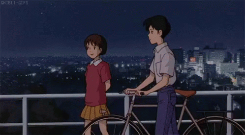 A Boy And A Girl Are Standing Next To A Bicycle On A Balcony Overlooking A City At Night . GIF