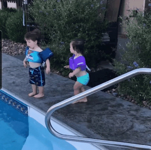 A Boy And A Girl Are Standing Next To A Pool Wearing Life Jackets GIF