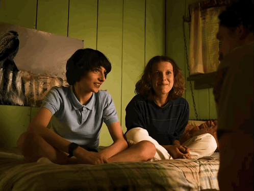 A Boy And A Girl Sit On A Bed In Front Of A Painting Of A Dog GIF