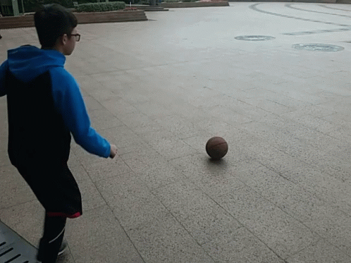 A Boy In A Blue Hoodie Is Kicking A Basketball On The Ground GIF
