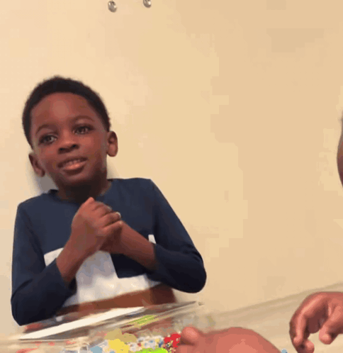 a boy in a blue shirt is clapping his hands in front of a cake