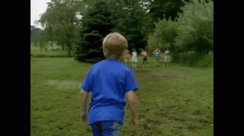 A Boy In A Blue Shirt Is Running In A Grassy Field GIF