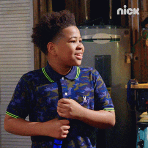 A Boy In A Camouflage Shirt Is Standing In Front Of A Water Heater With The Nick Logo On The Bottom GIF
