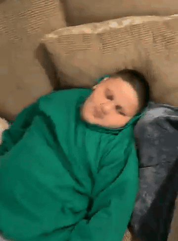 A Boy In A Green Hoodie Is Laying On A Couch . GIF