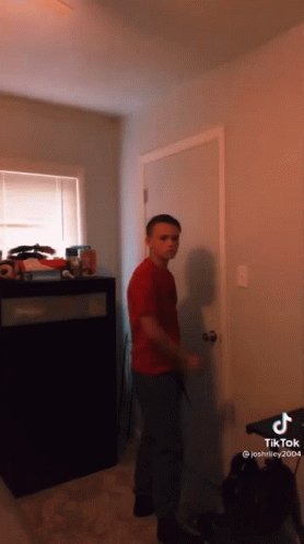 A Boy In A Red Shirt Is Standing In Front Of A Door In A Room GIF