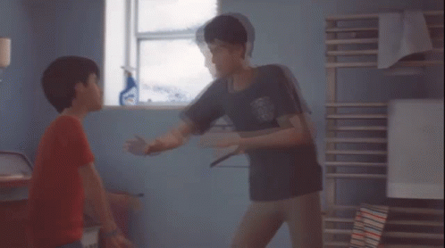 A Boy In A Red Shirt Is Standing Next To Another Boy In A Room GIF