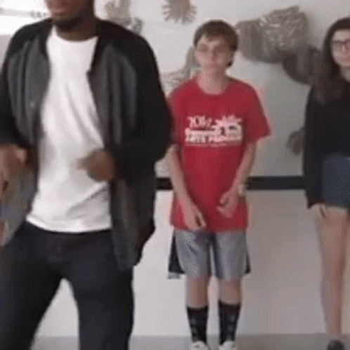 A Boy In A Red Shirt That Says X On It Is Standing Next To Two Other People GIF