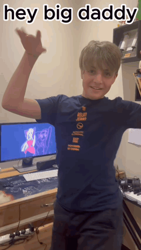 A Boy In A Relay Jeans Shirt Is Standing In Front Of A Computer Monitor GIF