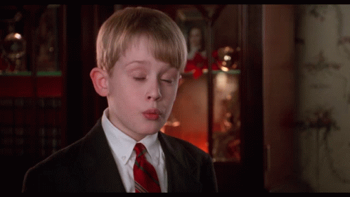 A Boy In A Suit And Tie Is Blowing A Kiss In Front Of A Bookcase GIF