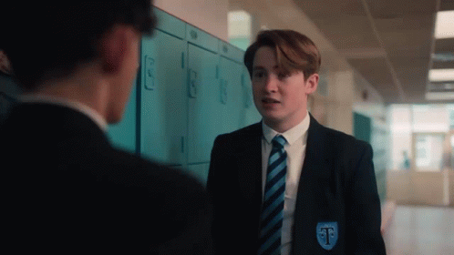 A Boy In A Suit And Tie Is Standing Next To A Boy In A Locker Room . GIF