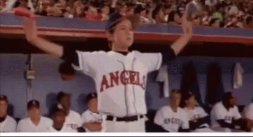 A Boy In An Angels Baseball Uniform Is Standing In Front Of A Crowd . GIF