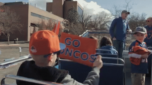 a boy in an orange hat holds up an orange sign that says go broncos