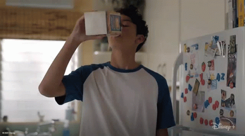 A Boy Is Drinking Milk From A Carton In Front Of A Disney + Fridge GIF