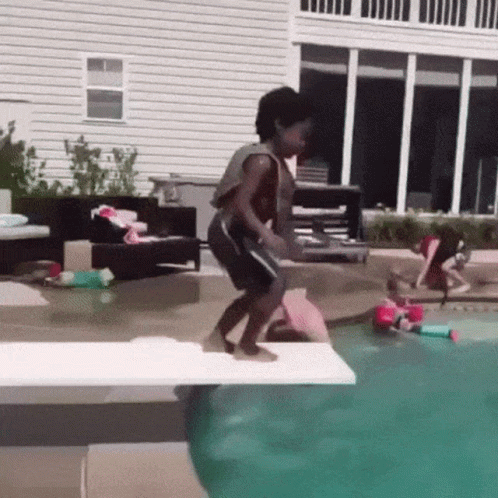 A Boy Is Jumping Into A Swimming Pool From A Diving Board . GIF