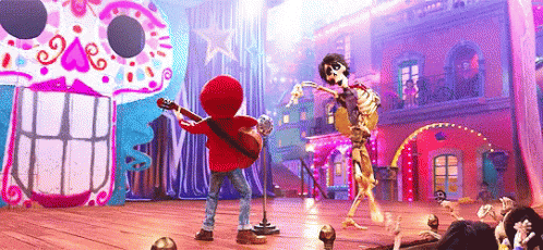 A Boy Is Playing A Guitar And Singing Into A Microphone While A Skeleton Is Dancing On A Stage . GIF