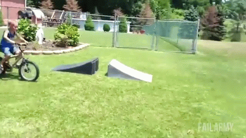 A Boy Is Riding A Bike Down A Ramp In A Grassy Field . GIF