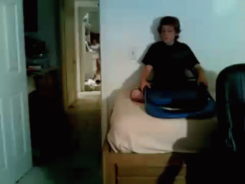 A Boy Is Sitting On A Bed Holding A Blue Suitcase GIF