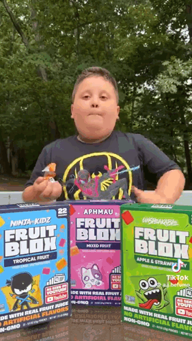 A Boy Is Standing In Front Of Three Boxes Of Fruit Blok . GIF