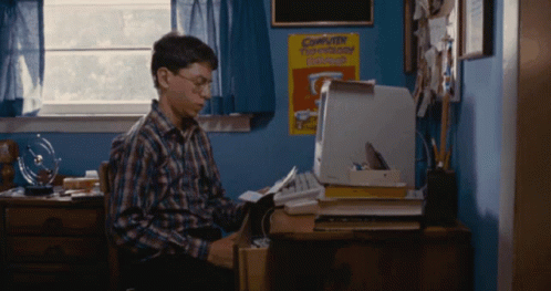 A Boy Sits At A Desk In Front Of A Computer And A Poster That Says Computer Technology Club GIF