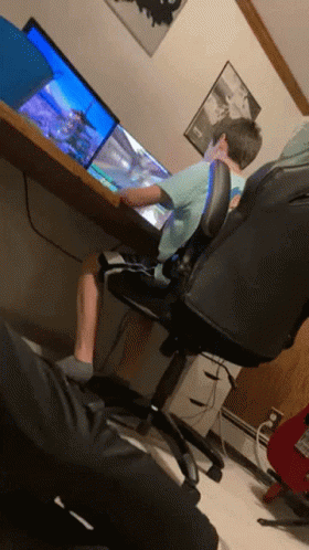 A Boy Sits At A Desk Playing A Video Game On A Computer GIF
