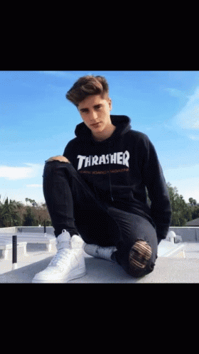A Boy Wearing A Black Thrasher Hoodie Sits On A Ledge GIF