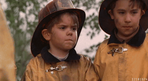 A Boy Wearing A Fireman 'S Helmet Is Standing Next To Another Boy Wearing A Fireman 'S Jacket GIF
