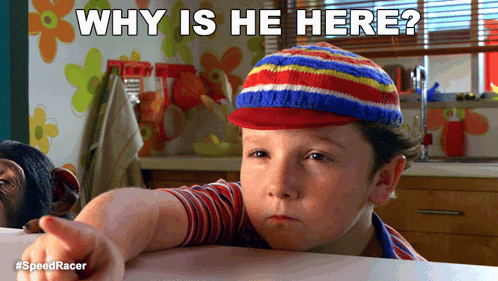 A Boy Wearing A Striped Hat Is Pointing At The Camera With The Caption " Why Is He Here " Above Him GIF