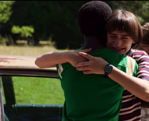 A Boy Wearing A Watch Is Hugging Another Boy In A Green Shirt GIF