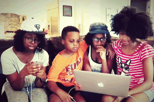 A Boy Wearing An Orange Shirt That Says Fun Is Looking At A Laptop GIF