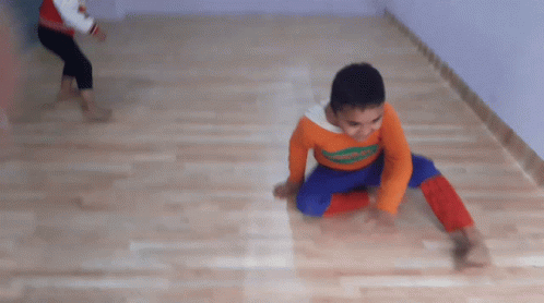 a boy wearing an orange shirt that says ' spiderman ' on it is doing a handstand on the floor