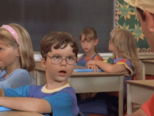 A Boy Wearing Glasses Is Sitting At A Desk In A Classroom GIF
