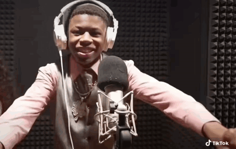 A Boy Wearing Headphones And A Pink Shirt Is Standing In Front Of A Microphone . GIF
