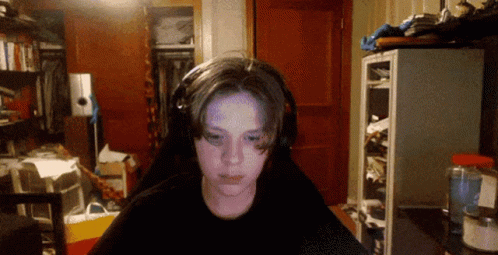 A Boy Wearing Headphones Looks At The Camera In A Cluttered Room GIF