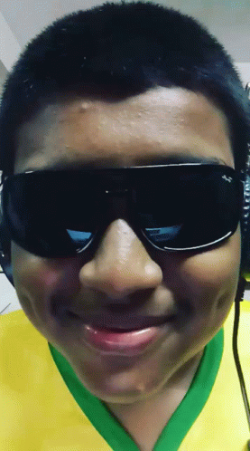 a boy wearing sunglasses and a yellow and green shirt smiles