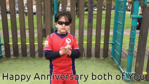 A Boy Wearing Sunglasses Stands In Front Of A Wooden Fence With The Words Happy Anniversary Both Of You GIF