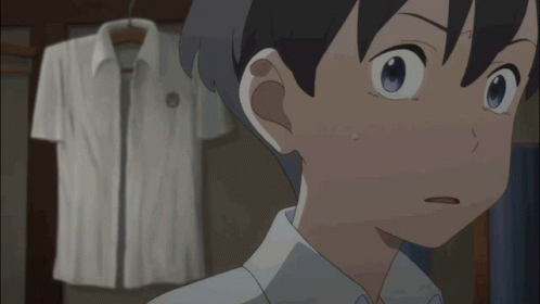 A Boy With A Surprised Look On His Face Stands In Front Of A White Shirt Hanging On A Rack GIF