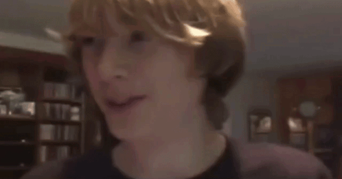 A Boy With Blonde Hair Is Smiling In A Dark Room GIF