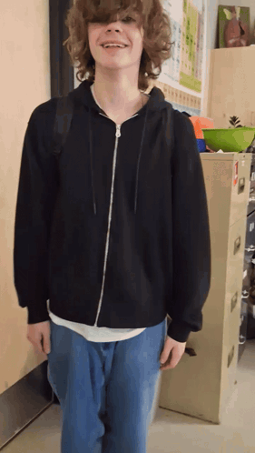 A Boy With Curly Hair Wearing A Black Hoodie And Jeans GIF