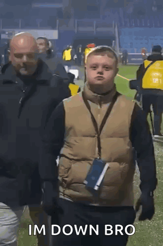 A Boy With Down Syndrome Is Walking On A Field With A Man Behind Him And Says Im Down Bro . GIF
