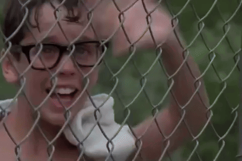 A Boy With Glasses Is Standing Behind A Chain Link Fence . GIF