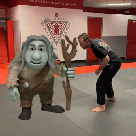 A Brazilian Jiu-Jitsu Practitioner Stands Next To A Troll In A Gym GIF