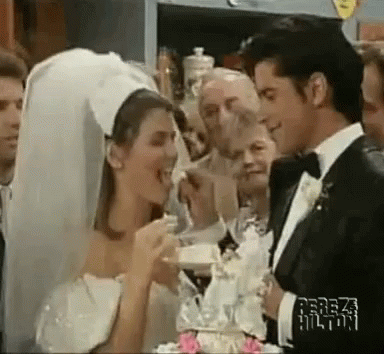 A Bride And Groom Are Cutting Their Wedding Cake While A Group Of People Watch . GIF