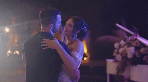 A Bride And Groom Are Dancing In Front Of A Piano In A Dark Room GIF