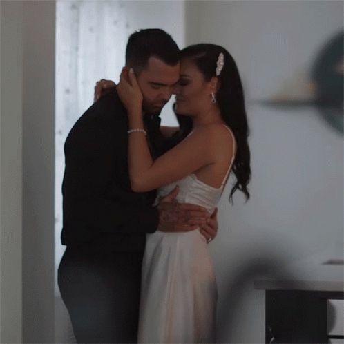 A Bride And Groom Are Hugging And Kissing In A Hallway GIF